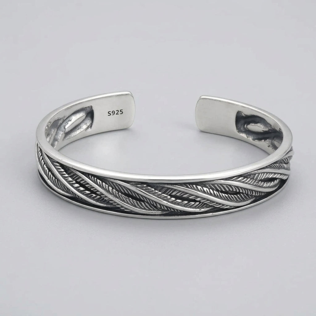 Silver bracelet with feather design on a gray surface