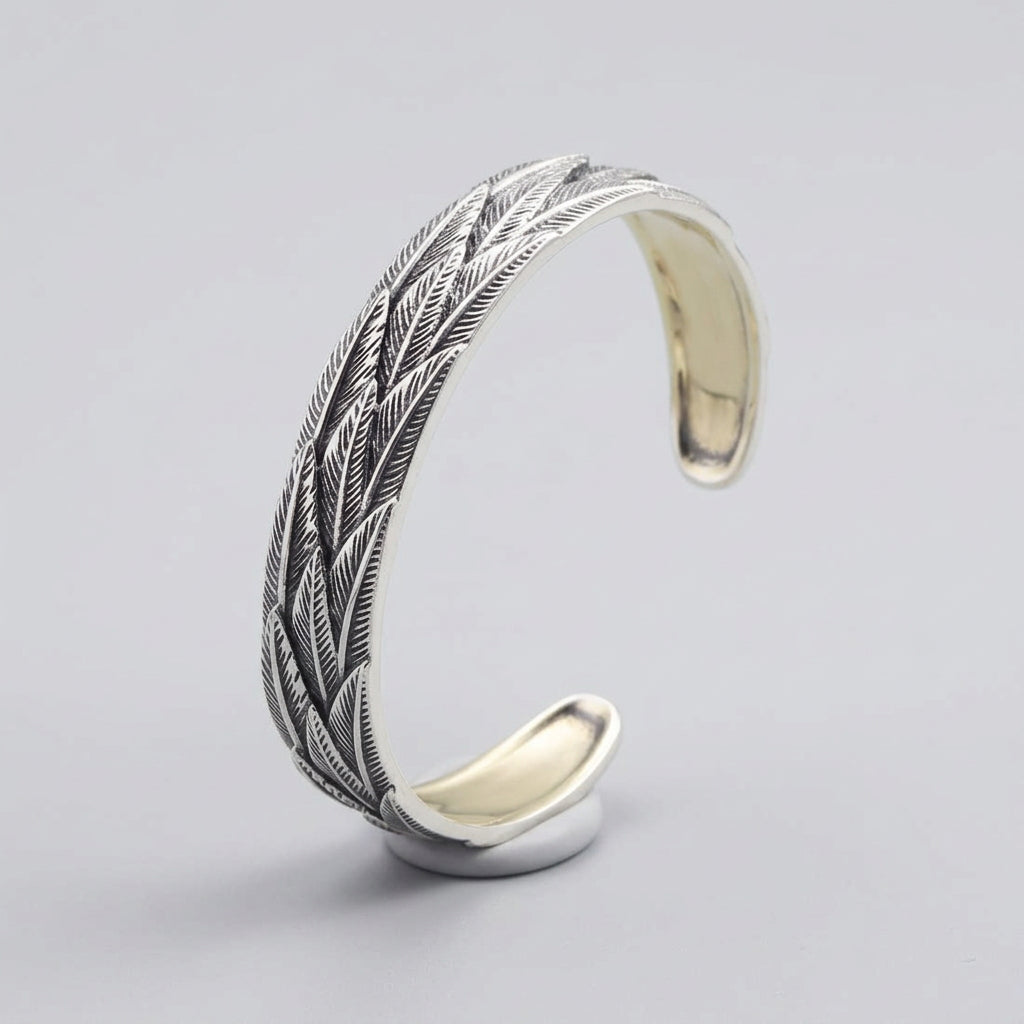 Silver feather-patterned bracelet on a wooden surface with a dark background