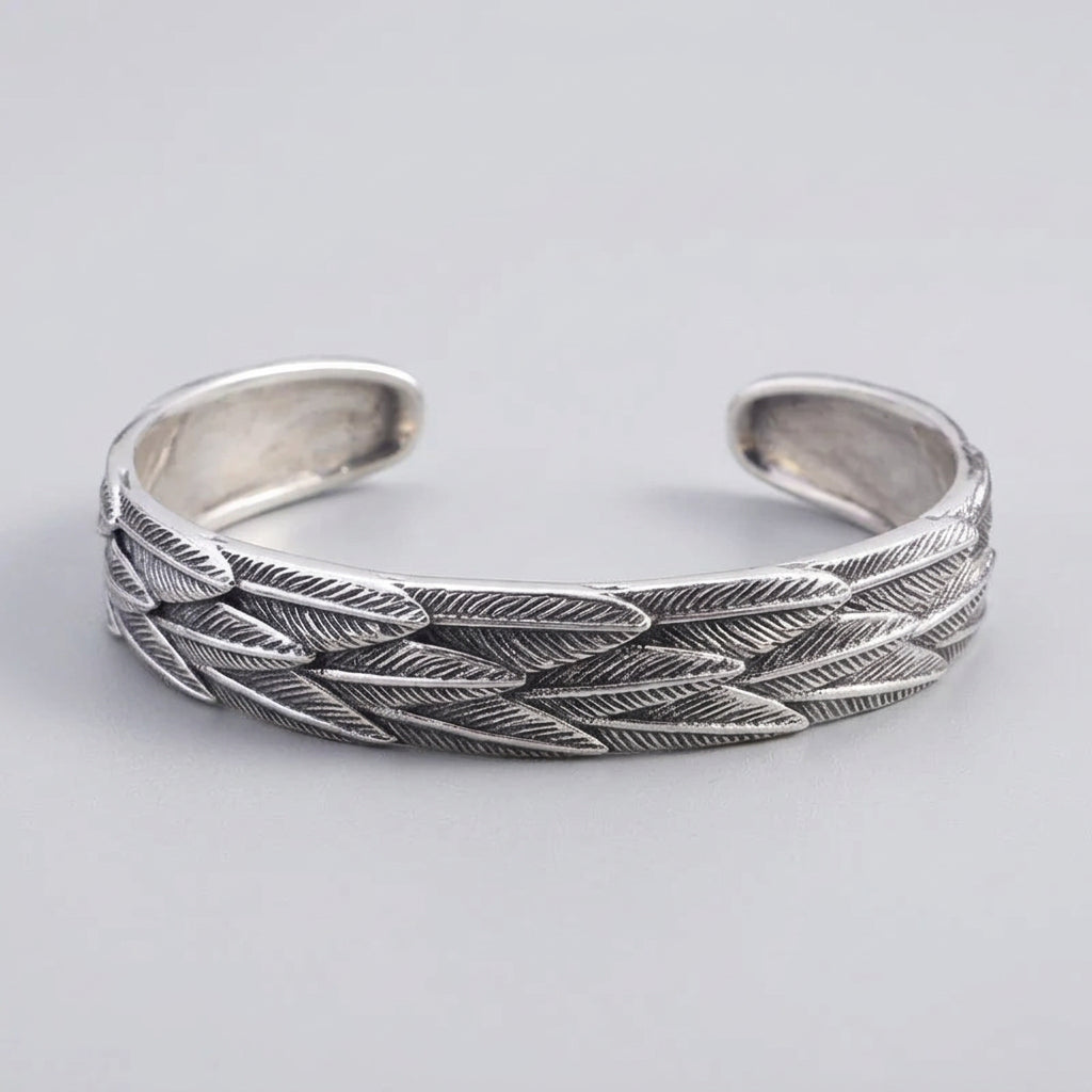 Silver feather-patterned bracelet on a wooden surface with a dark background