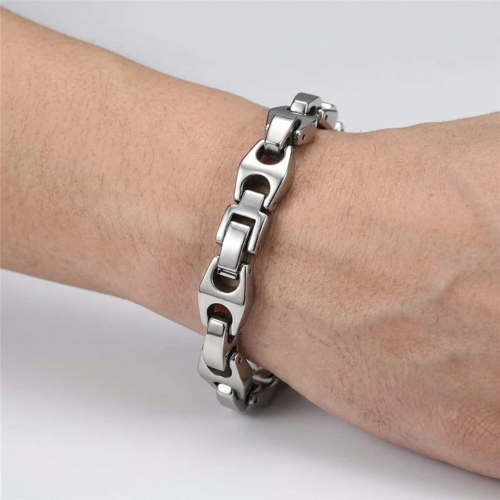 A close-up of a silver stainless steel chain link bracelet worn on a person's wrist, paired with a black leather jacket and dark shirt cuff.