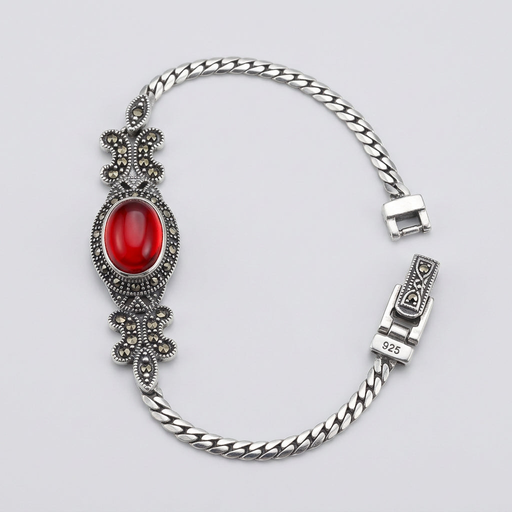 Silver bracelet with a red gemstone on a wooden surface